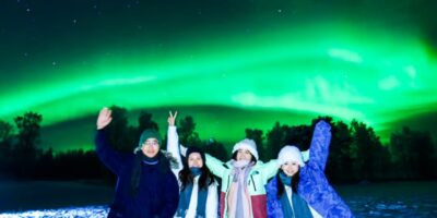 Aurora Borealis over a snowy Arctic landscape in Rovaniemi, Finland, with a tour group watching the Northern Lights.