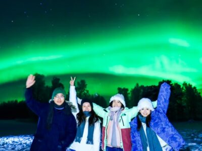 Aurora Borealis over a snowy Arctic landscape in Rovaniemi, Finland, with a tour group watching the Northern Lights.