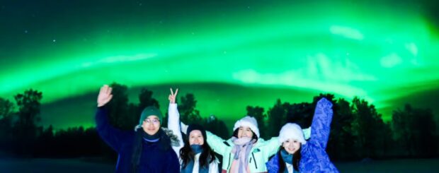 Aurora Borealis over a snowy Arctic landscape in Rovaniemi, Finland, with a tour group watching the Northern Lights.