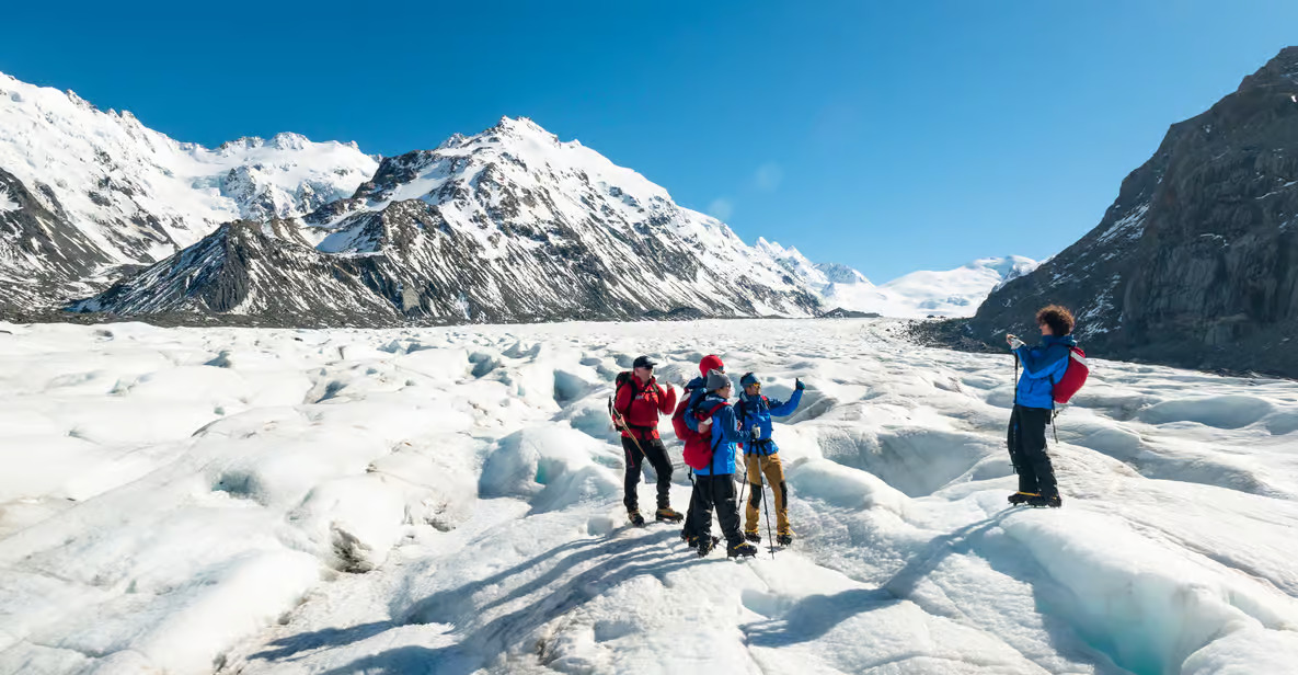 A scenic helicopter flying over the stunning Tasman Glacier in Mount Cook National Park, with hikers exploring the icy terrain below