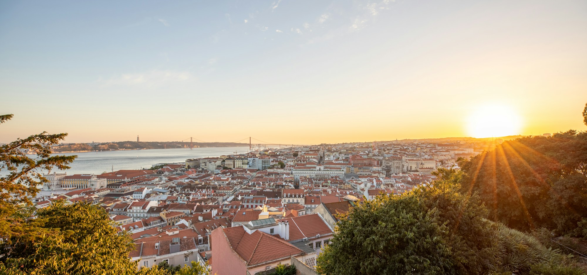 Golden evening light over Lisbon’s rooftops and the Tagus River.